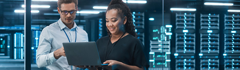 A woman and man looking at a laptop with a large server room in the background