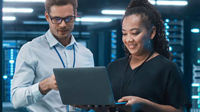 A woman and a man looking at a laptop with a large server room in the background