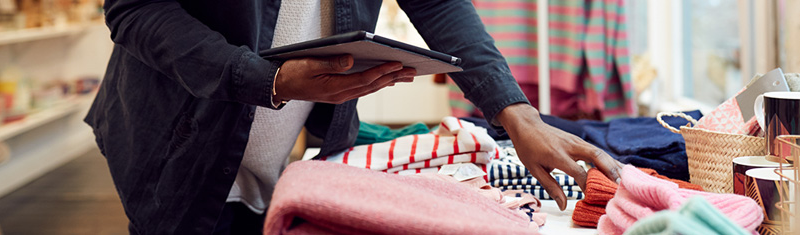 A person holding a tablet looking at clothes in a shop