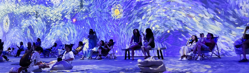 People inside a room with art projected on walls and floor
