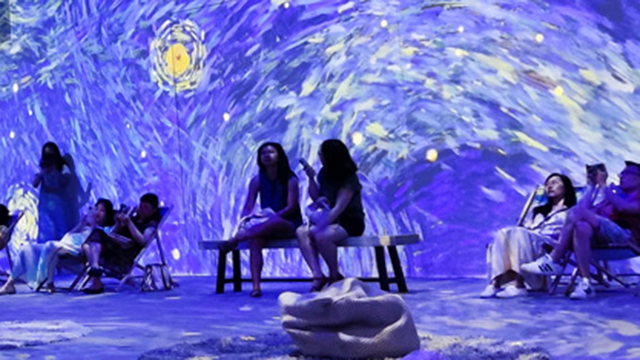 People inside a room with art projected on walls and floor