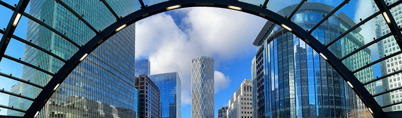 A daytime view of a glass arch with office buildings in the background