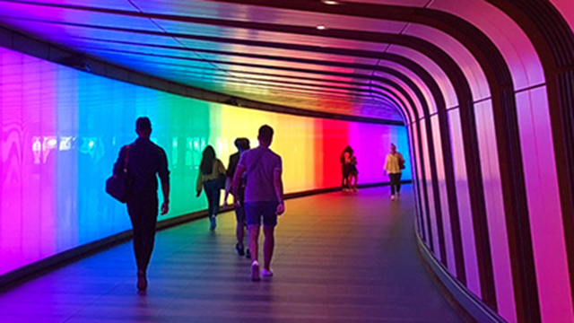 People walking through the multicolour-illuminated Kings Cross light tunnel