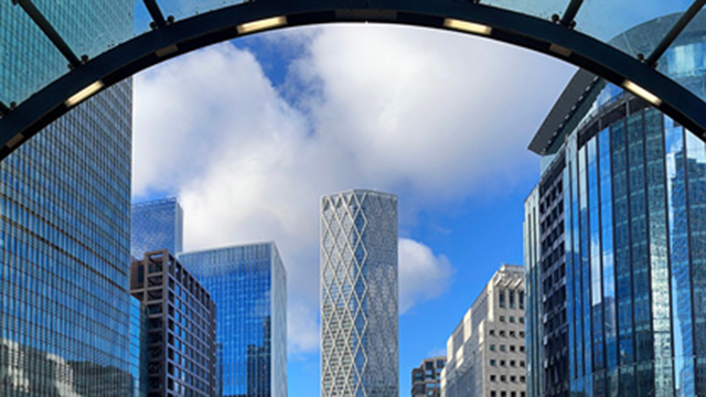 A daytime view of a glass arch with office buildings in the background