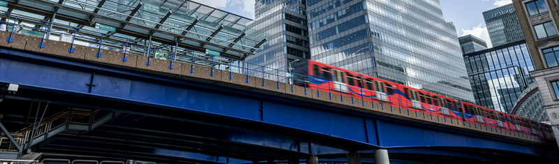 A daytime view of a rail bridge with the DLR passing next to office buildings