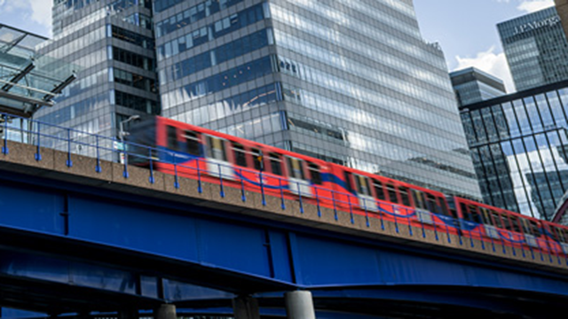 A daytime view of a rail bridge with the DLR passing next to office buildings