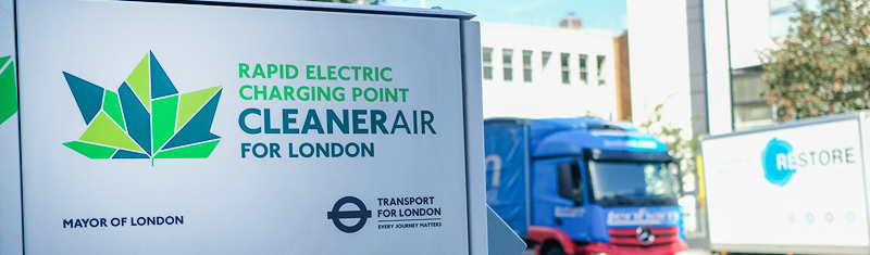 A billboard that reads rapid electric charging point, cleaner air for London with lorry in the background.