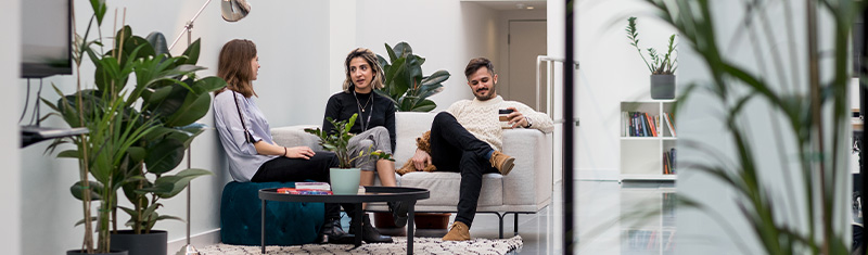 Three colleagues sat on a sofa having a conversation in an office space.