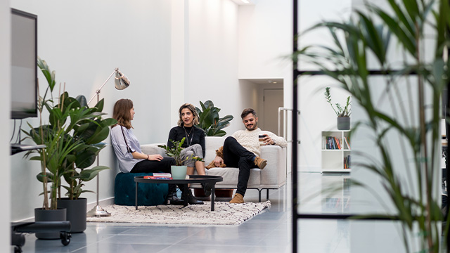 Three colleagues sat on a sofa having a conversation in an office space.