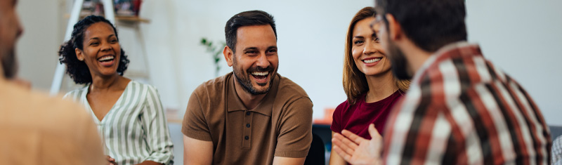 A group of people sitting in a circle in an office talking and smiling.