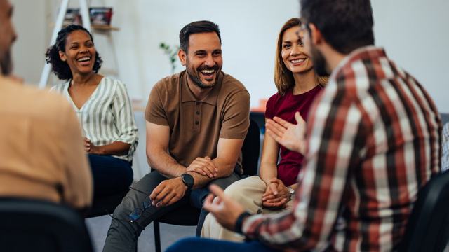 A group of people sitting in a circle in an office talking and smiling.