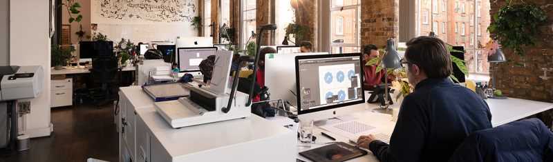 A view of a modern office space with people working on desktop computers.