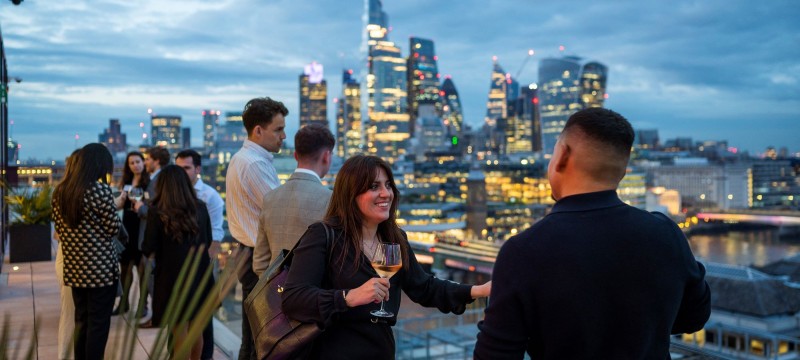 A group of young professionals chat in front of the London skyline.